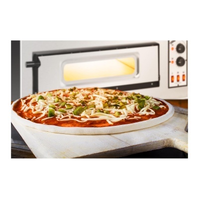 Pizza crua com queijo e pimento verde numa pá de madeira em frente a forno de pizza