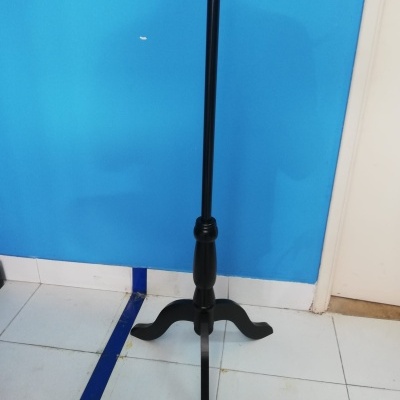 Suporte de madeira preta para instrumento ou microfone com base tripé em chão de azulejos brancos e parede azul