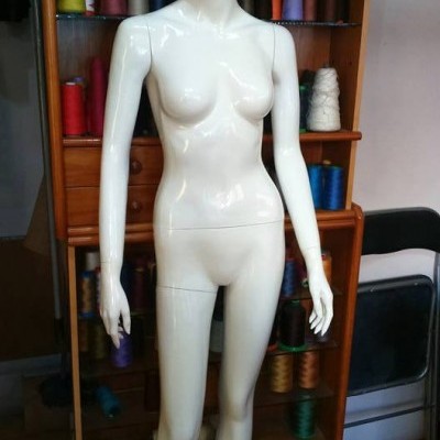 Mannequim feminino branco com bobinas de linha colorida ao fundo.