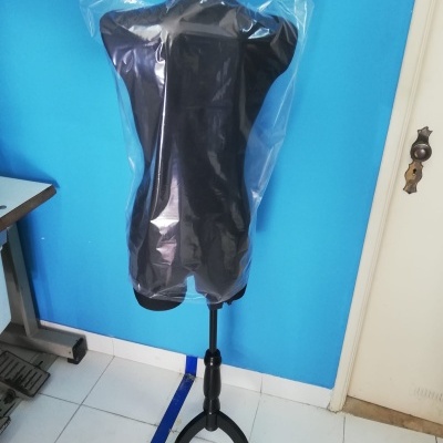 Mannequim preto com capa plástica numa sala com parede azul