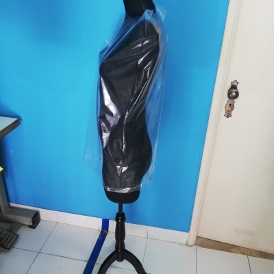 Manequim preto com capa plástica numa sala com parede azul