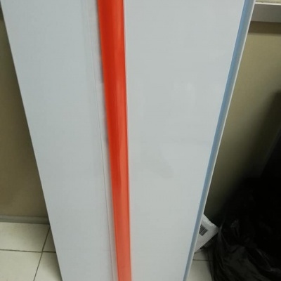 Prancha branca vertical com objeto cilíndrico laranja apoiado à sua frente em chão de azulejos claros