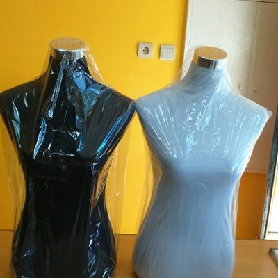 Dois manequins de torso em plástico preto e branco cobertos com plástico transparente sobre mesa de madeira clara junto a parede amarela