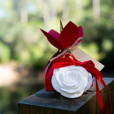 Caixa vermelha em forma de flor com etiqueta e rosa branca decorativa com fita vermelha sobre madeira