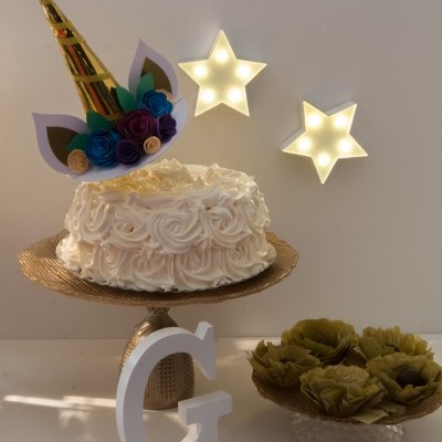 Bolo branco decorado com creme, chifre dourado e flores de papel, estrelas luminosas e letra decorativa G