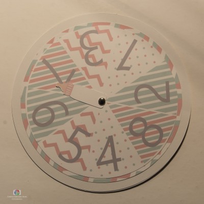 Relógio de parede redondo com padrões geométricos coloridos e números grandes cinzentos