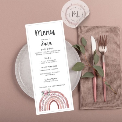 Menu de batizado em papel branco com texto e arco-íris, sobre prato cinza com talheres rosas e guardanapo castanho claro