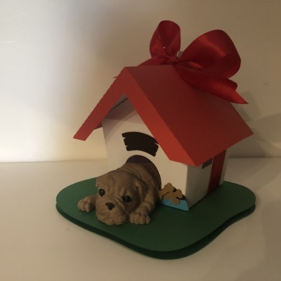 Figura decorativa de cão deitado à entrada de casinha com telhado vermelho