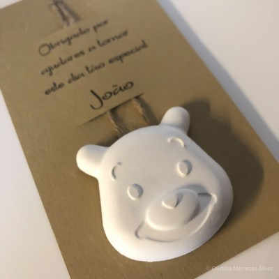 Objeto decorativo branco em forma de rosto de urso sobre cartão castanho com texto manuscrito