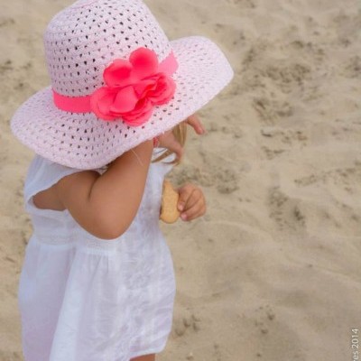 Criança na praia com vestido branco e chapéu branco com flores rosa