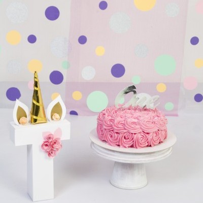 Bolo rosa decorado com rosa e número 1 decorado como unicórnio sobre fundo com círculos coloridos