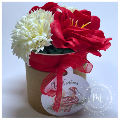 Arranjo floral artificial com flores vermelhas e brancas em vaso castanho com fita vermelha e pendente natalício.