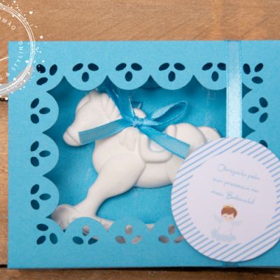 Caixa azul com cavalo de cerâmica branco e etiqueta de batizado.