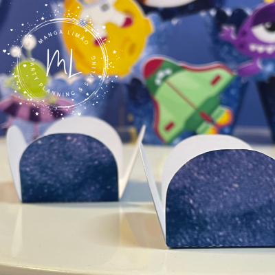 Caixinhas pequenas de papel branco com interior azul escuro pontilhado sobre mesa branca e decoração colorida ao fundo