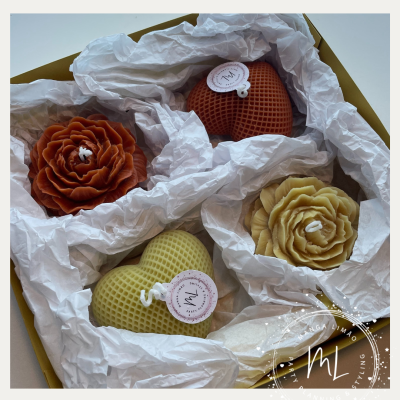Velas decorativas em caixa dourada com papel branco, em formas de flores castanha e bege e corações castanho e amarelo com etiquetas.