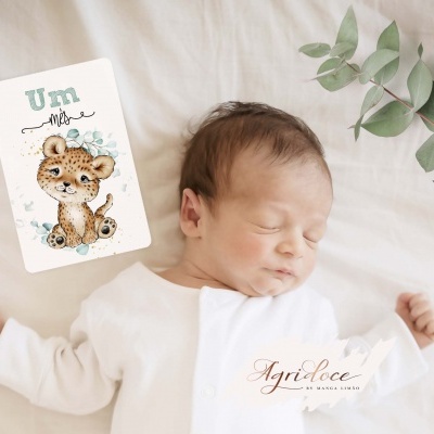 Bebé a dormir de branco com cartão a indicar um mês e ramo verde ao lado