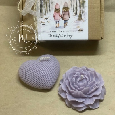Duas velas lilás decorativas em forma de coração e flor ao lado de caixa com ilustração de crianças e texto em inglês.