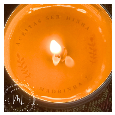 Vela laranja acesa em vidro com texto 'ACEITAS SER MINHA MADRINHA'