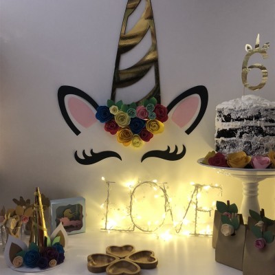 Decoração de festa de unicórnio com bolo, letras luminosas e flores de papel coloridas