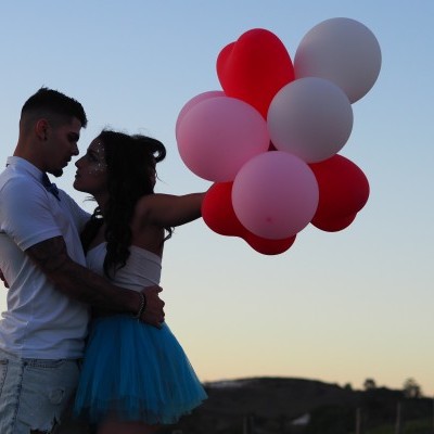 Casal abraçado ao ar livre com balões coloridos ao entardecer