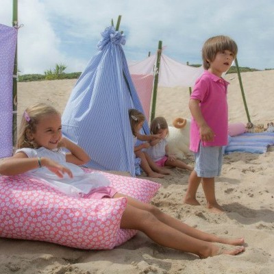 Crianças na praia com tenda azul e almofadas cor-de-rosa na areia