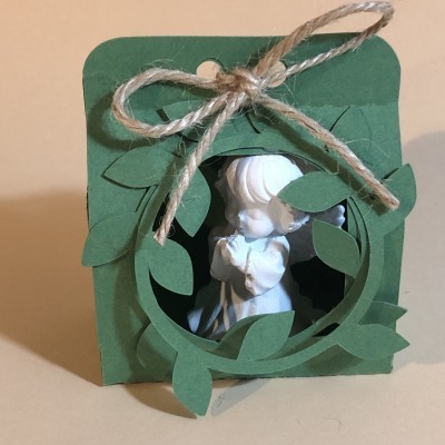 Anjo branco em pose de oração dentro de embalagem verde decorada com folhas e laço de corda