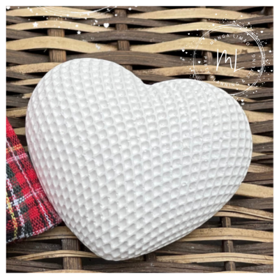 Almofada branca em formato de coração com textura em relevo sobre vime