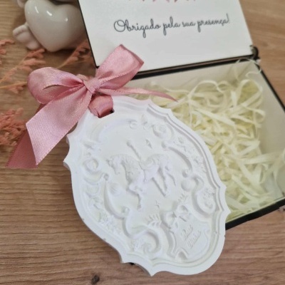 caixa decorativa aberta com cartão e medalhão com laço rosa, em superfície de madeira
