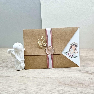 Convite artesanal com fita e selo de cera ao lado de anjo branco ajoelhado.