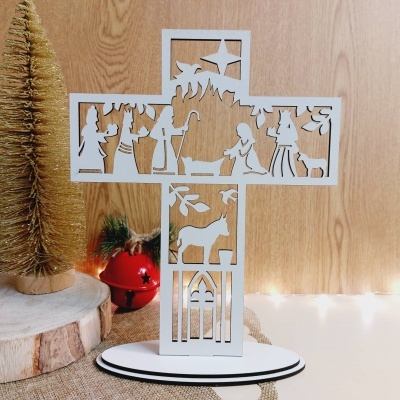 Escultura branca em forma de cruz com recortes natalícios numa mesa de madeira