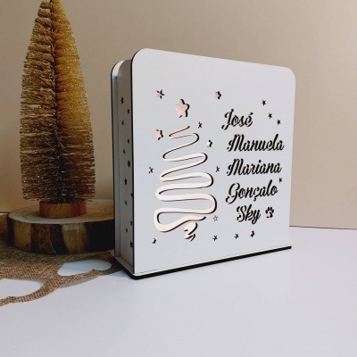 Caixa metálica branca com recortes de árvore de Natal e nomes em preto
