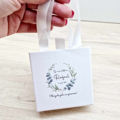 Embalagem branca quadrada com alça e texto decorativo para batismo
