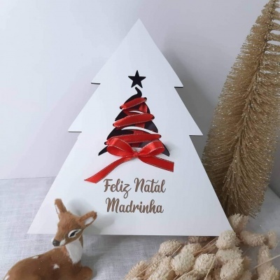 Decoração de Natal branca em forma de árvore com fita vermelha e texto 'Feliz Natal Madrinha', veado de peluche castanho e enfeites dourados