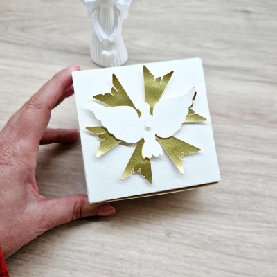 Caixa branca com pomba decorativa em relevo dourado e branco segurada por uma mão
