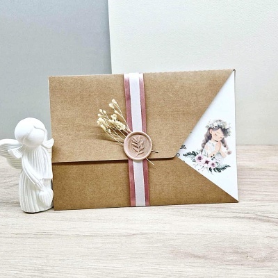 Envelope castanho com fita rosa e branca, selo de cera, ramo seco e cartão ilustrado com rapariga