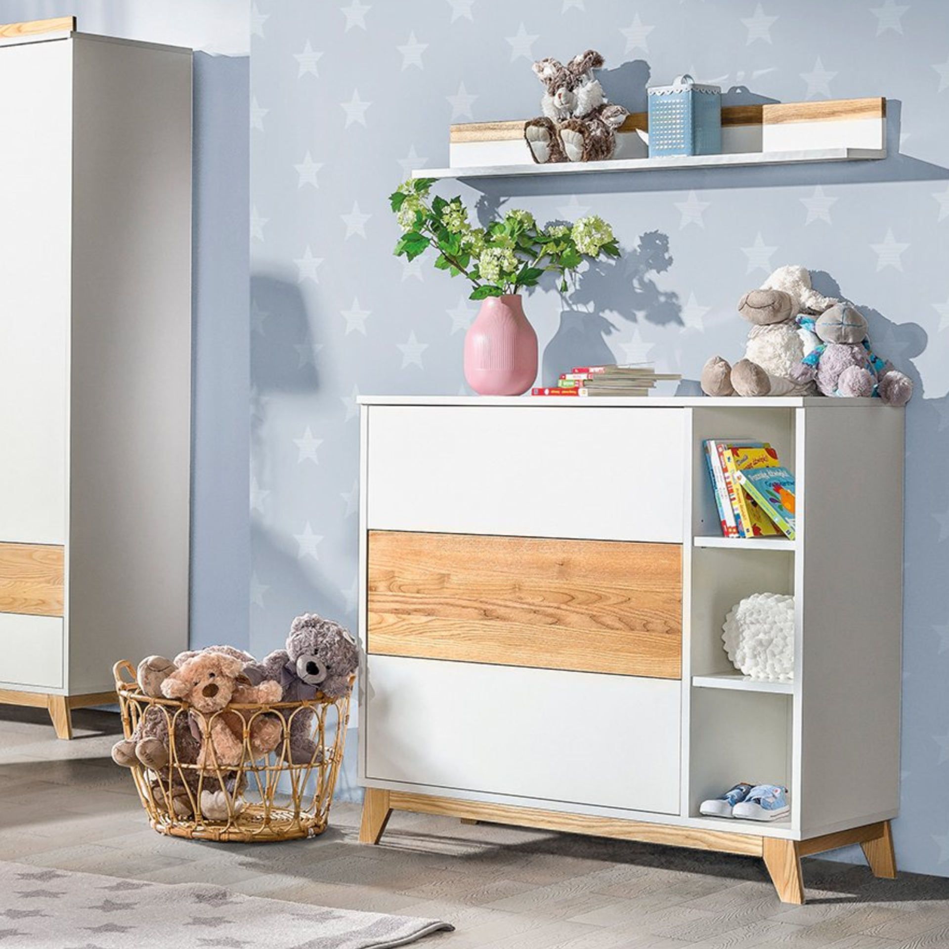 Cómoda com Trocador e Gavetas NORDIK Cómoda branca com detalhes em madeira e peluches num quarto infantil com papel de parede azul com estrelas