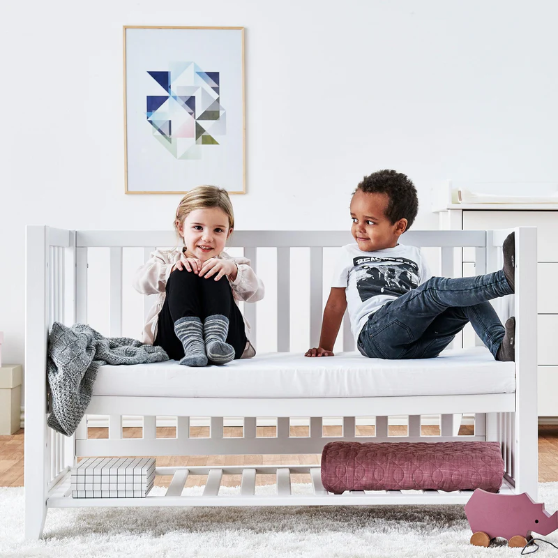 Colchão de Espuma para Berço e Cama de Grades Berço branco de madeira com crianças sentadas e cobertor cinza na lateral