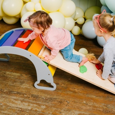 Duas crianças brincando numa estrutura de madeira colorida com bolas ao fundo