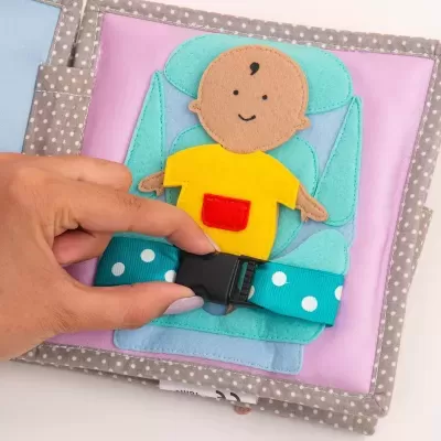 Livro de tecido com ilustração de bebé e cinto azul com pontos brancos