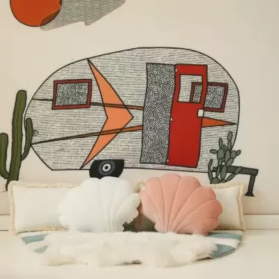 Almofadas em forma de conchas em frente a uma parede com pintura de caravana colorida