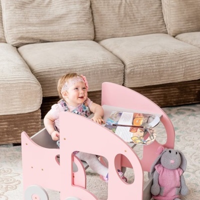 Carrinho de brincar rosa com criança, livros e coelho de malha ao lado
