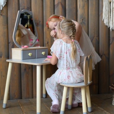 Secretária e cadeira infantil de madeira com espelho, numa sala com parede de madeira e decoração rústica.