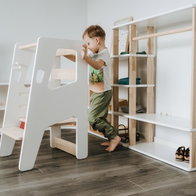 Criança a usar escadote infantil branco em ambiente interior com prateleiras e plantas