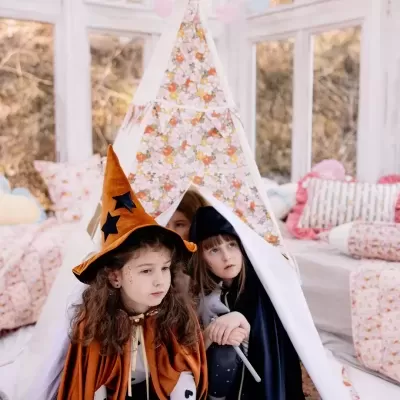 Tenda tipi branca com padrão floral e duas crianças vestidas de bruxas sentadas dentro