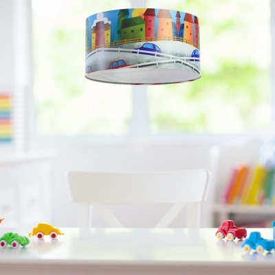 Abajur colorido com padrão de casas e carros, carrinhos de brinquedo coloridos numa mesa branca