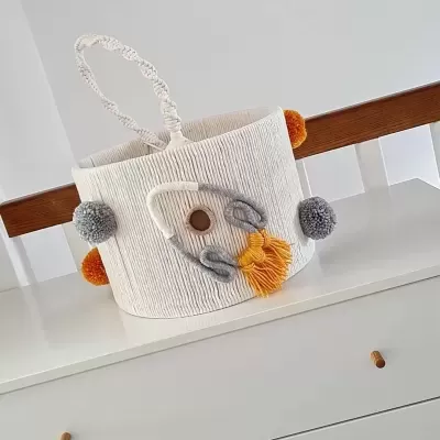 Cesto decorativo branco com pompons e aplicação de foguete em tecido sobre móvel branco