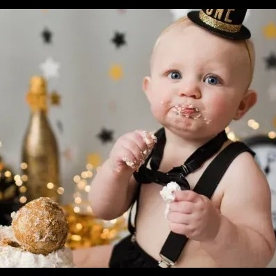 Bebé com chapéu e suspensórios a comer bolo em ambiente festivo com decoração de estrelas