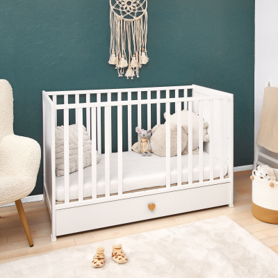 Berço branco com colchão e peluches em quarto com parede verde e cadeira bege