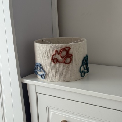 Cesto de tecido bege com desenhos coloridos de carros, em cima de móvel branco