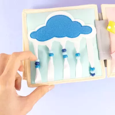 Livro sensorial de tecido com nuvem azul e tiras brancas com contas azuis